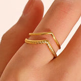 Gold Chevron Serenity ring on a finger against a beige background