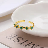 Gold open ring with green gemstones on a white dish